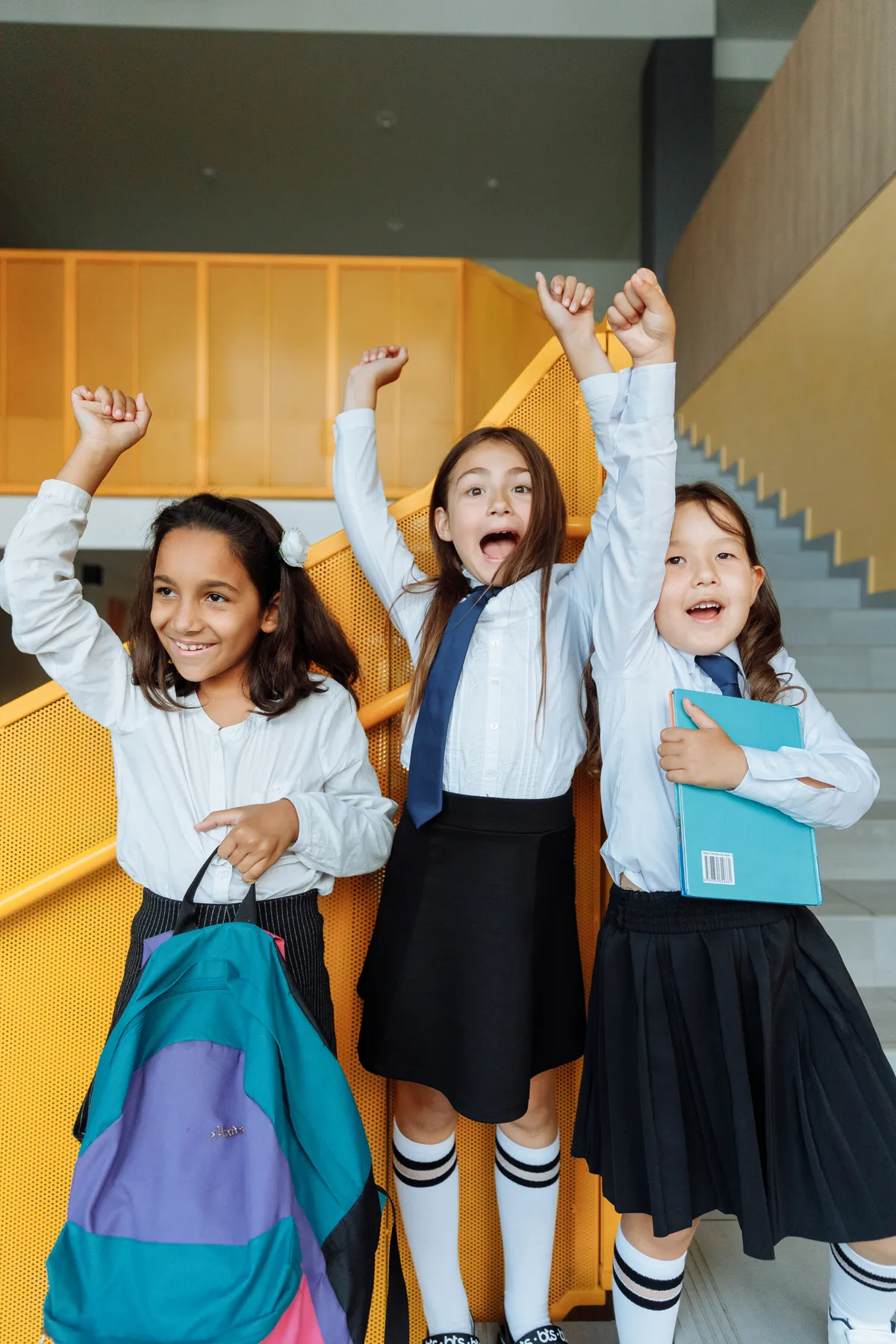Three cheerful schoolchildren in uniform celebrating together